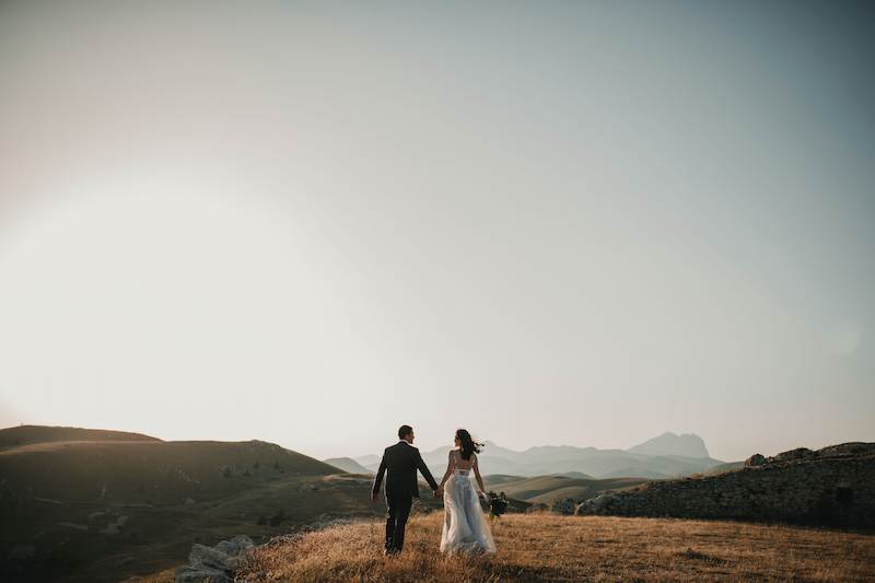 A married couple stands on a hill.